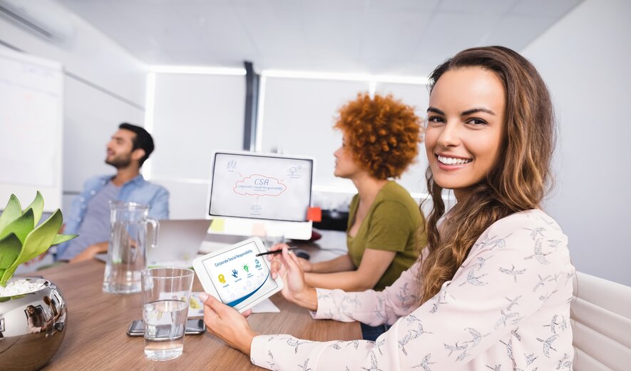 Frau im Büro mit Tablet und Team bei der Projektdiskussion.
